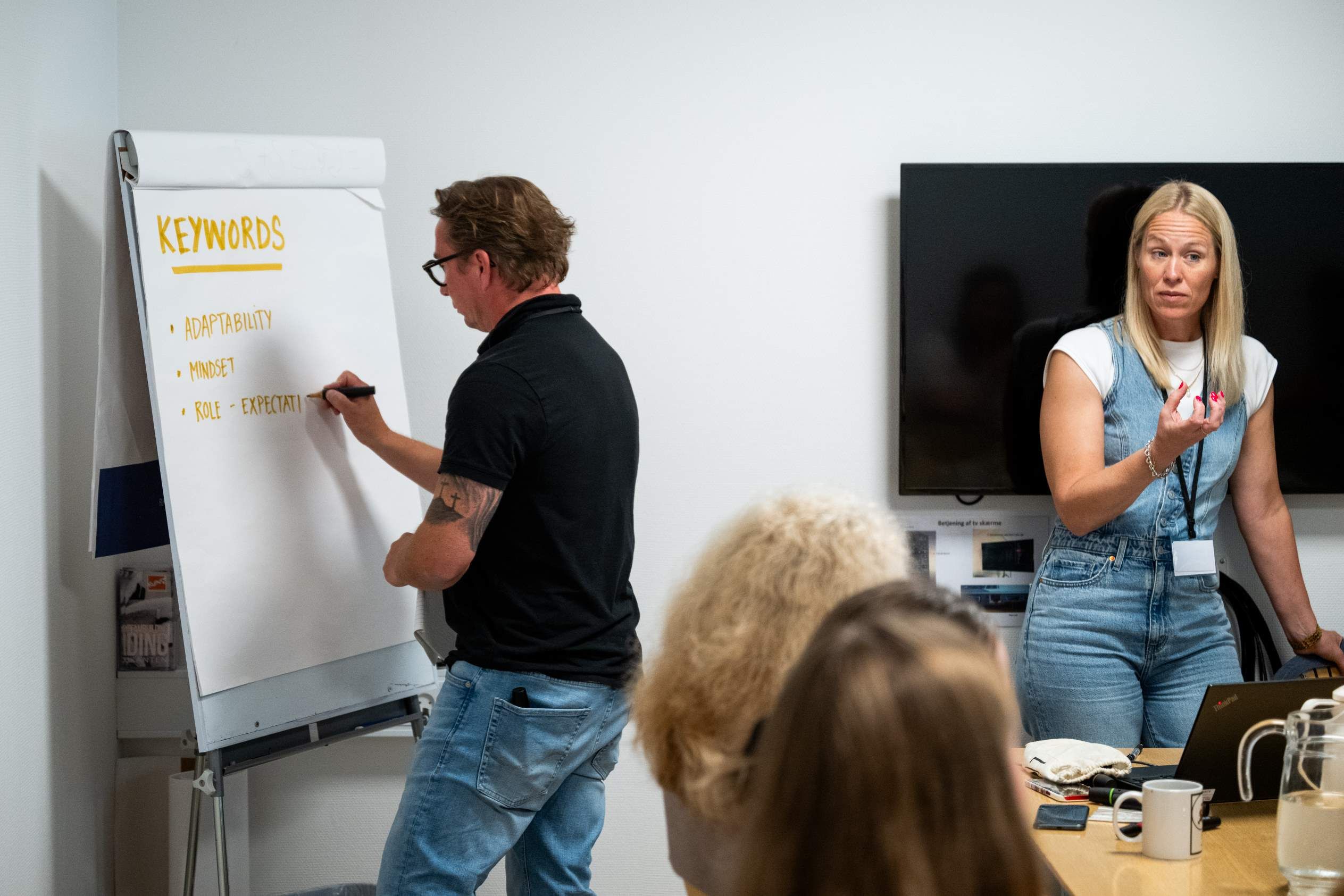 Marie Fink faciliterer en workshop, mens en deltager skriver på en flipover